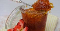 a jar filled with jam sitting on top of a table next to a pink flower