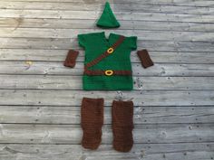 a knitted elf outfit with brown pants and green hat sitting on top of a wooden floor