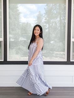 a woman standing in front of a window wearing a white and blue dress with stripes