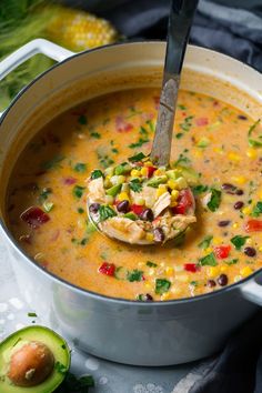 a spoon full of soup with corn, black beans and avocado on the side