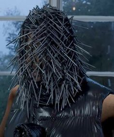 a woman with spiked hair and black leather jacket in front of a window looking out the window