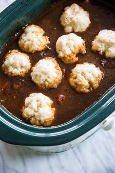 a green casserole dish filled with meat and dumplings