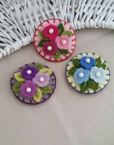 three small flower brooches sitting on top of a white cloth covered table next to a wicker basket