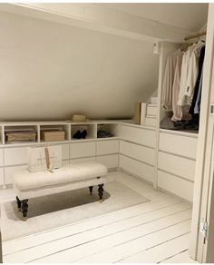 a white bench sitting in the middle of a room next to a closet filled with clothes