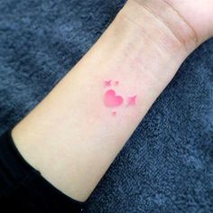 a small pink heart tattoo on the wrist