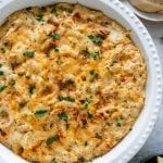 a casserole dish with cheese and herbs in it on a table next to bread