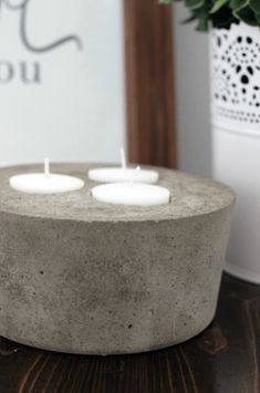 three lit candles sitting on top of a cement container next to a potted plant