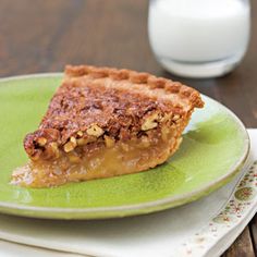 a piece of pie on a green plate next to a glass of milk and fork