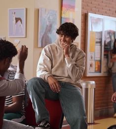 a man sitting on top of a red chair next to other people in a room