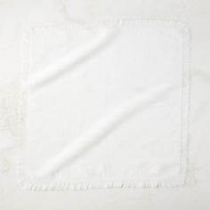 a white napkin with fringe edges on a plain surface, viewed from the top down