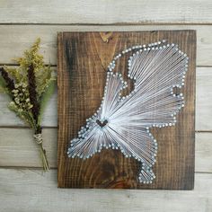 a string art piece is displayed on a wooden surface next to dried flowers and twigs