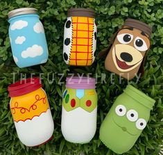 four different colored mason jars sitting on top of some green grass with cartoon characters painted on them