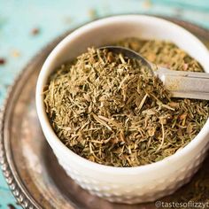 a white bowl filled with dried herbs on top of a metal tray next to a spoon