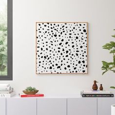 a white and black painting hanging on the wall next to a plant in a vase