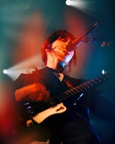 a woman holding a guitar in front of a microphone and some lights on the stage