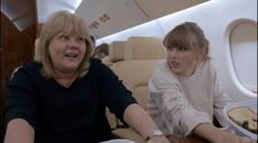 two women sitting at a table with food in front of them on an airplane aisle