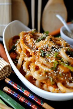 a bowl filled with noodles and vegetables next to chopsticks on a table top