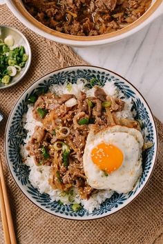 two bowls filled with rice and meat next to chopsticks on a table top