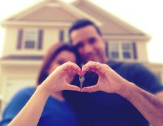 a man and woman making a heart shape with their hands in front of a house