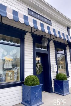 two large blue planters are in front of the store's windows and awnings