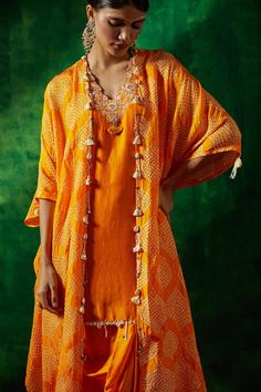 Kesar silk cape with bandhani print and mirror embroidered collar. Comes with a chanderi dhoti skirt and a kurta.
Components: 3
Pattern: Printed, Embroidered
Type Of Work: Bandhani, Mirror
Neckline: V Neck
Sleeve Type: Cape : Flared Sleeves, Kurta : Sleeveless
Fabric: Chanderi, Cape : Silk
Color: Yellow,Orange
Other Details: 
Tassel detailing on cape
Occasion: Sangeet - Aza Fashions Bohemian Straight Kurta Sets For Festive Occasions, Bohemian Sets With Gota Work For Navratri, Bohemian Sets With Gota Work For Festivals, Bohemian Art Silk Sets For Navratri, Bohemian Cutdana Salwar Kameez For Festivals, Bohemian Art Silk Sharara For Designer Wear, Bohemian Chanderi Sets For Festive Occasions, Bohemian Style Art Silk Kurta For Festivals, Festive Bohemian Chanderi Palazzo Set