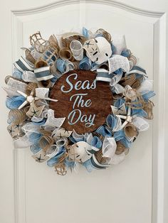 a wreath that says seas the day hanging on a white door with blue and beige ribbons