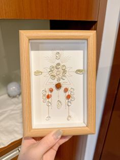 a person holding up a framed artwork in front of a wooden cabinet with jewelry on it