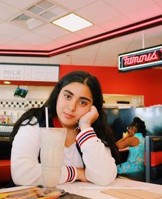 a woman sitting at a table with a milkshake in front of her face