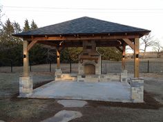 a gazebo with stone pillars and an open fire place in the middle of a field