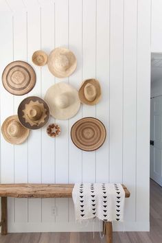 several hats are hanging on the wall above a wooden bench in front of a white painted wall