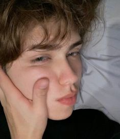 a young man laying in bed with his hand under his chin and looking at the camera