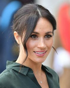 a close up of a person wearing a green shirt and smiling at the camera with her hair pulled back