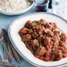 a white plate topped with meatballs and peas next to silverware on a blue table cloth