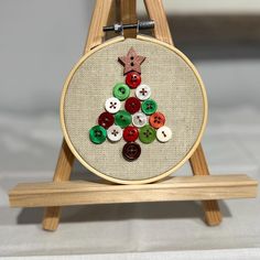 a wooden easel holding a cross stitch christmas tree ornament with buttons on it