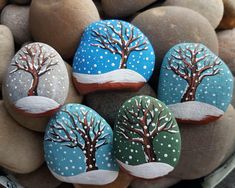 four painted rocks with trees on them sitting on top of some rocks covered in snow