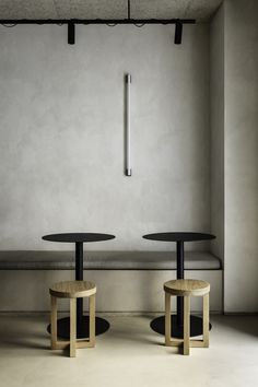 two round tables sitting next to each other in front of a white wall and concrete floor