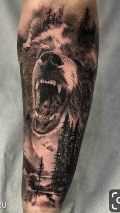 a man's arm with a bear and forest scene tattoo on the left forearm