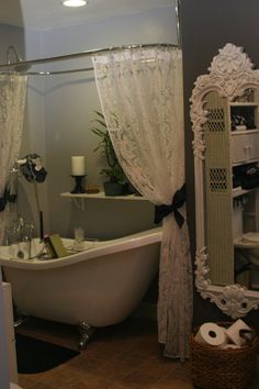 an old fashioned bathtub and toilet in a bathroom with lace curtains on the window