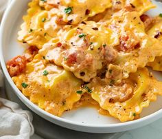 a white plate topped with ravioli and meat covered in cheese on top of a marble table