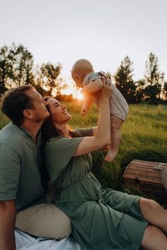 a man and woman are sitting on the grass with a baby in their lap, as the sun sets behind them