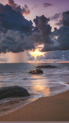 the sun is setting over the ocean with clouds in the sky and rocks on the beach