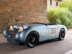 an old blue sports car parked in front of a brick wall with numbers on it