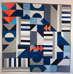 a blue and orange quilt hanging on a wall next to a white wall with an abstract design