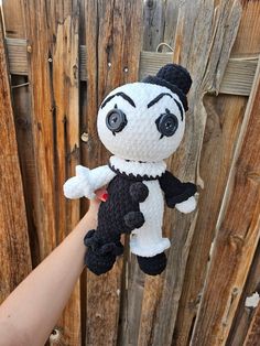 a hand holding a small stuffed animal in front of a wooden fence with planks