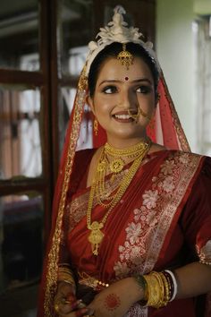 a woman in a red and gold bridal outfit with jewelry on her face smiling