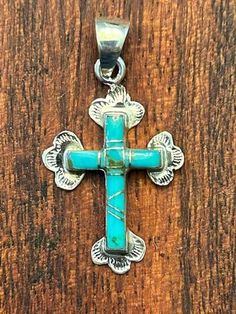 A delicate 1 3/8" tall sterling silver and turquoise inlay cross pendant.   Turquoise is inlaid in this sweet cross and set with bands of sterling silver.  An attached bail makes it ready to wear on a chain, cord or neck ring. Measures 1 3/8" in height, 3/4" in width. 28977 Turquoise Cross Ring, Adjustable Turquoise Cross Jewelry, Southwestern Blue Cross Jewelry, Southwestern Style Blue Cross Jewelry, Turquoise Sterling Silver Cross Pendant, Turquoise Sterling Silver Cross Pendant Jewelry, Artisan Sterling Silver Crucifix Jewelry, Southwestern Silver Cross Jewelry, Silver Turquoise Cross Necklace For Gift