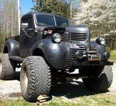 an old black truck parked on top of a grass covered field with trees in the background