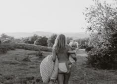 a woman carrying a baby in her arms while walking through the grass with an umbrella over her head