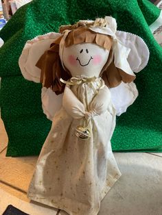 a cloth doll is sitting on the floor next to a green blanket and pillow that has been folded over it