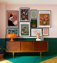 a room with pictures on the wall and a dresser in front of it that has an orange lamp next to it